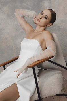 a woman in a white dress sitting on a chair with her arms behind her head