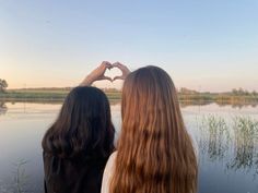 two women standing next to each other holding their hands in the shape of a heart