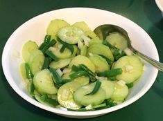 a white bowl filled with sliced cucumbers and green onions next to a spoon