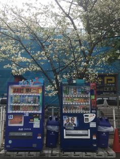 two vending machines sitting next to each other near a tree