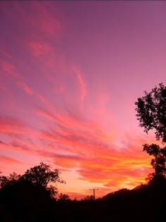 the sky is pink and purple as the sun sets in the distance behind some trees