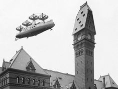 an airplane flying over a large building with a clock on it's front and side