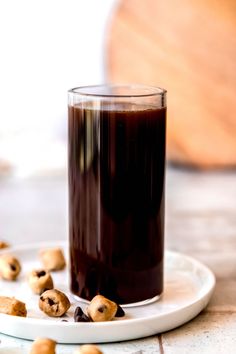 a glass filled with liquid sitting on top of a white plate next to some nuts