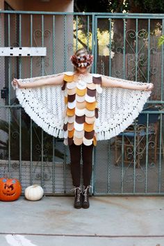 a woman standing in front of a gate with her arms spread out, wearing a dress made from strips of yarn