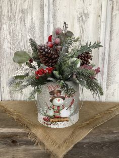 a christmas arrangement in a glass vase on a burlap tablecloth with pine cones and evergreens