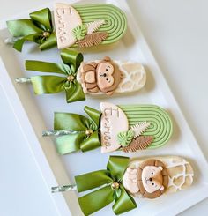 three decorated cookies with green ribbons on a white tray, one has a monkey and the other is a giraffe