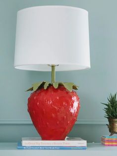 a red vase sitting on top of a table next to a white lampshade