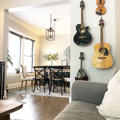 a living room filled with furniture and guitars hanging on the wall next to a table