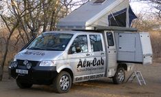 a van parked in front of some trees with a camper attached to the back