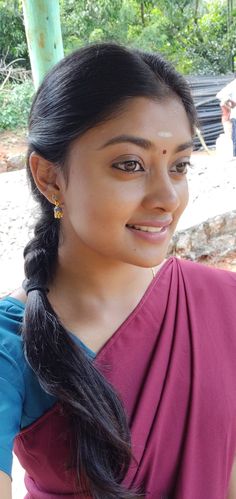 a woman in a pink sari smiling at the camera with her hair pulled back