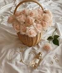 a basket filled with pink roses sitting on top of a white bed next to a bottle