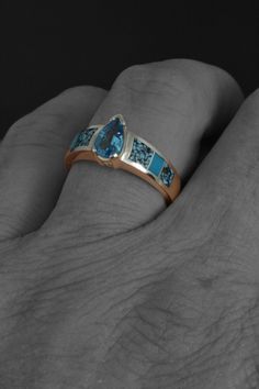 a person's hand with a gold and blue stone ring on it, in front of a black background