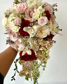 a bridal bouquet is being held by a woman's hand with red and white flowers