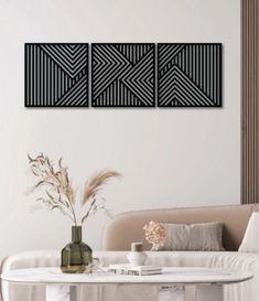 three black and white paintings on the wall above a table with flowers in vases