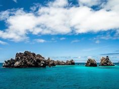 an island in the middle of the ocean with rocks sticking out of it's water