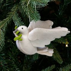 a white bird ornament hanging from a christmas tree with green leaves on it