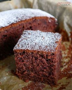 a chocolate cake with powdered sugar on top is cut in half and sits on a piece of parchment paper