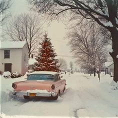 an old car parked in front of a christmas tree on a snowy street with snow