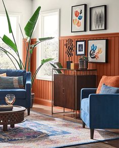 a living room with blue couches and wooden paneling on the walls, an area rug in between two windows