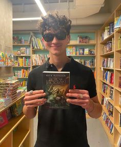 a young man holding up a book in front of a library filled with children's books