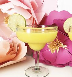 two margaritas with lime slices on the rim and flowers in the background, sitting next to each other