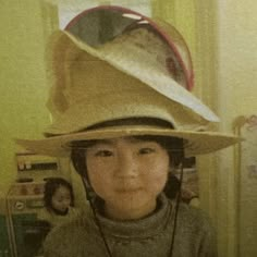 a young boy wearing a hat with two hats on top of his head, and another person in the background