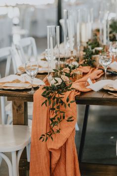 the table is set with orange linens and greenery