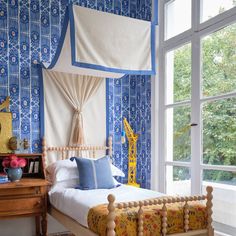 a bedroom with blue and white wallpaper, wooden bed frame, and large window