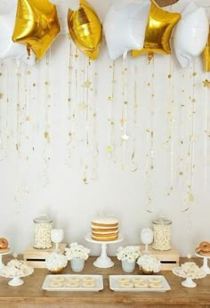 the dessert table is set up with gold and white balloons hanging from the ceiling above it