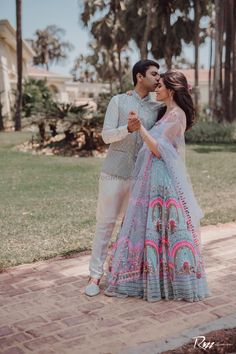 a man and woman standing next to each other on a brick walkway in front of palm trees