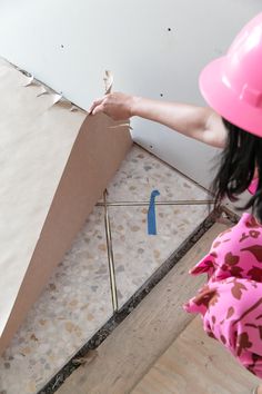 a woman wearing a hard hat and pink shirt standing next to a cardboard box on the floor