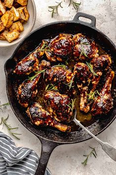 a skillet filled with chicken wings and garnished with fresh herbs, next to a bowl of potatoes