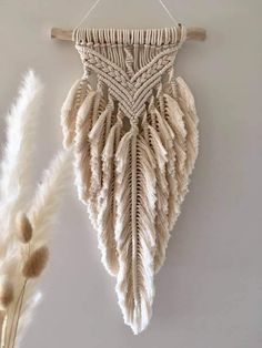 a wall hanging made out of yarn and feathers on a white wall next to dried flowers