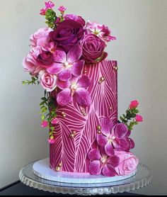 a pink and purple cake with flowers on top is sitting on a glass platter