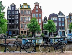 three bikes parked next to each other on the side of a river with buildings in the background