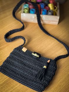 a black crocheted purse sitting on top of a wooden table next to yarn