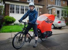 a man on a bicycle with an umbrella attached to the back wheel, in front of some houses