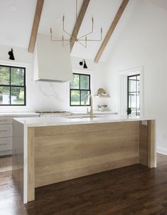 a kitchen with white walls and wooden floors, an island countertop and two windows