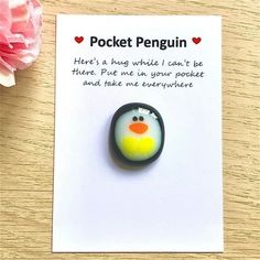 a penguin brooch sitting on top of a piece of paper next to a pink flower