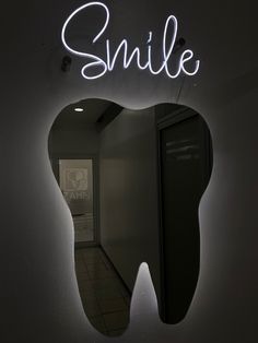 a tooth shaped mirror with the word smile lit up on it's side in front of a white wall