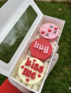 a person holding a box filled with cupcakes that say hug and kiss me