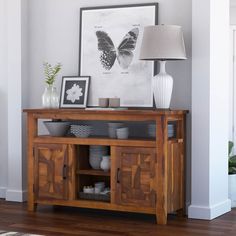 a wooden table topped with bowls and vases next to a framed butterfly print on the wall