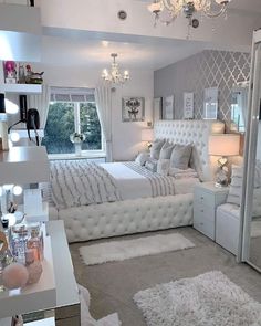 a large white bed sitting in a bedroom under a chandelier next to a window