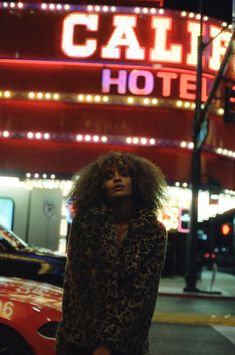 a woman standing on the street in front of a building with neon signs and lights