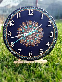 a blue clock sitting in the grass on top of a wooden stand with numbers around it