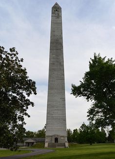 an obelisk stands in the middle of a grassy area with trees around it