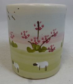 a ceramic cup with sheep and flowers painted on it's sides, sitting on a white surface