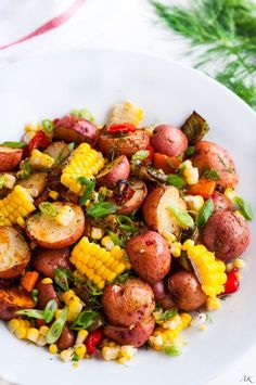 a white plate topped with potatoes, corn and green garnish on top of a table