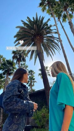 two women standing next to each other in front of palm trees with the sky behind them