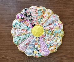 a multicolored flower design placemat on a wooden table with a yellow center piece